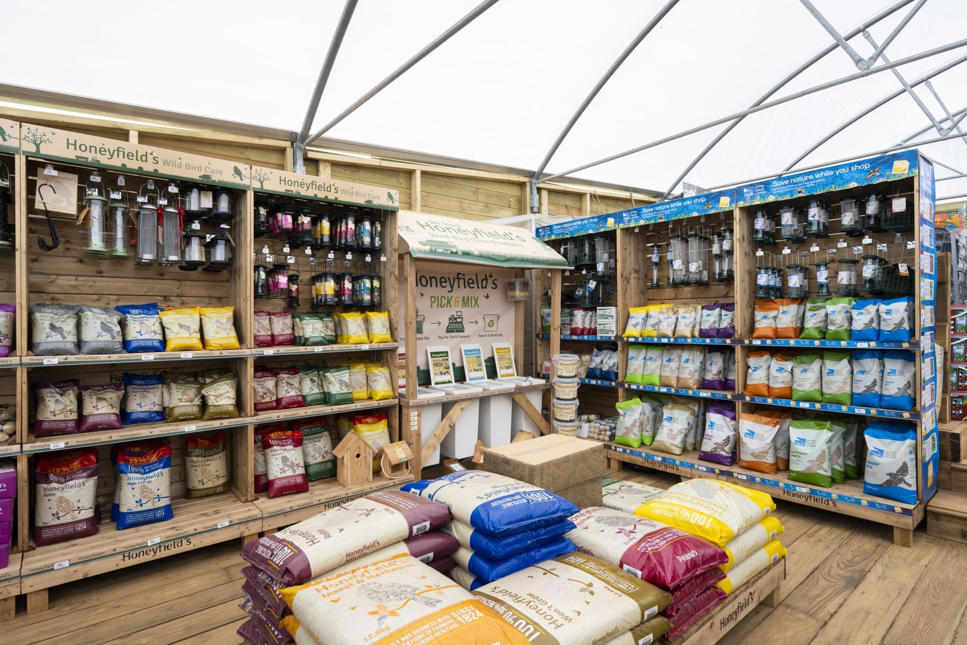 Shelves of pet food and supplies in a store. Various colored bags of food, wooden fixtures, overhead lighting.
