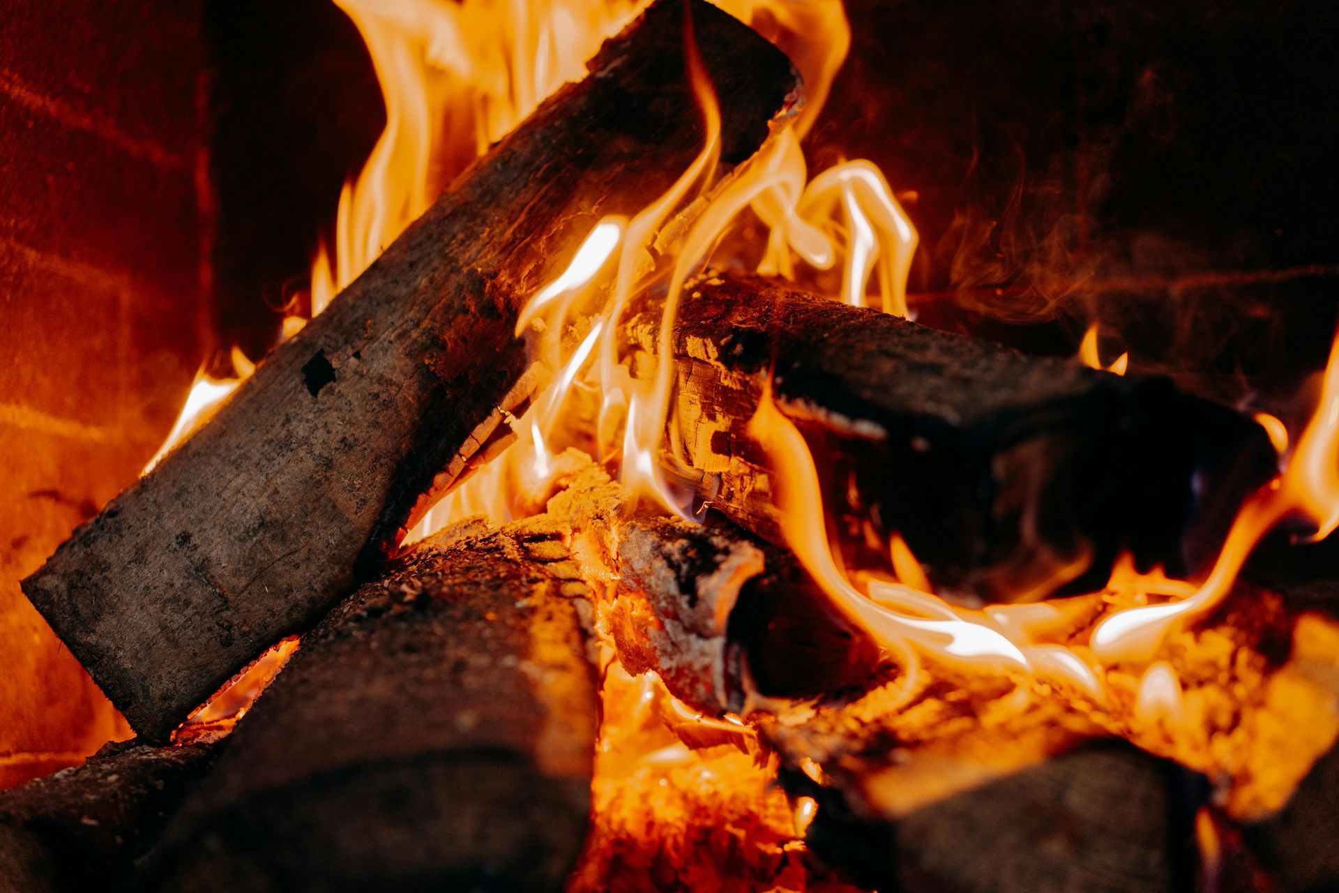 Burning logs in a fireplace, flames are orange and yellow, brick interior.