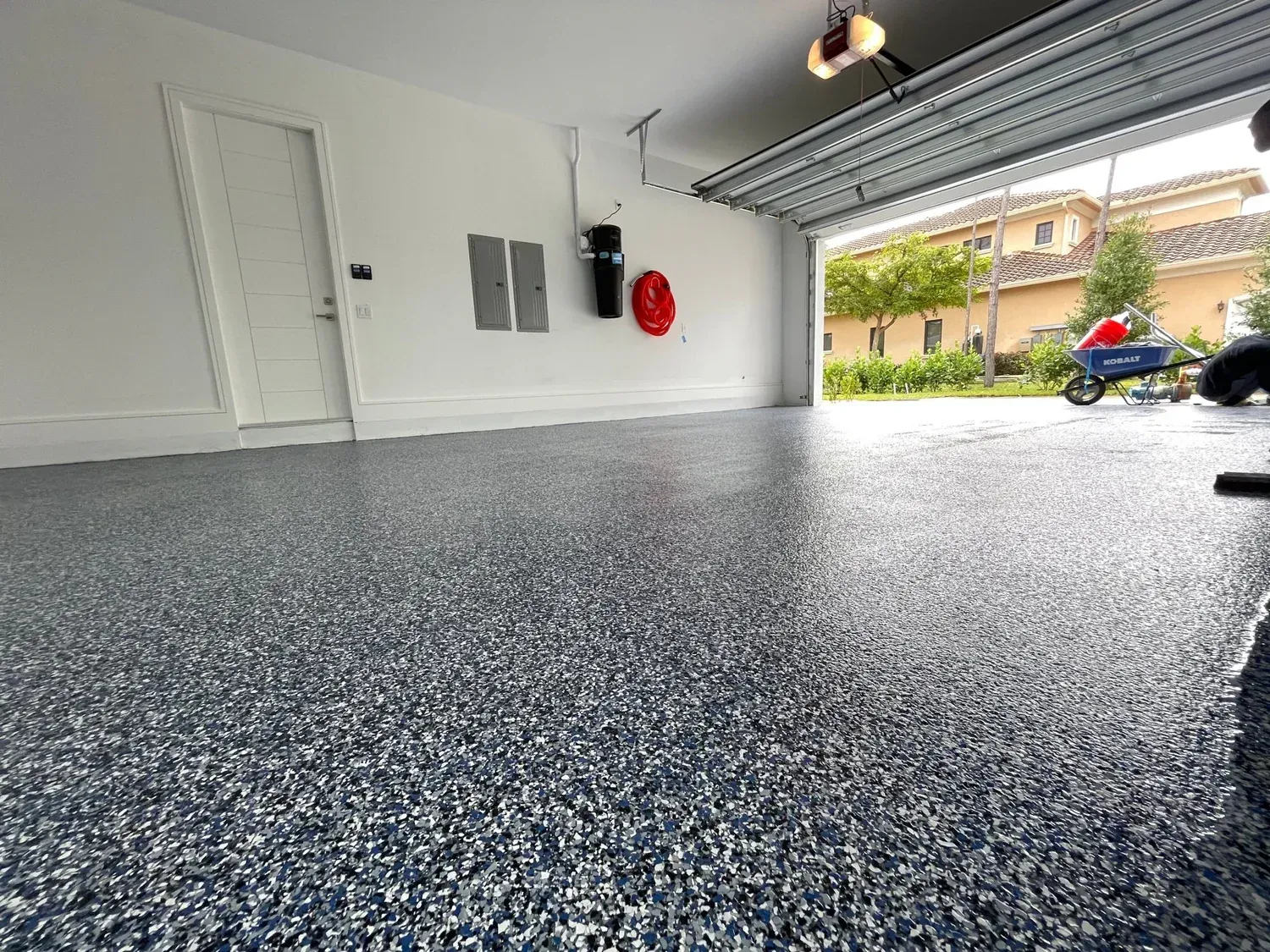 A garage with a concrete floor and a garage door open.