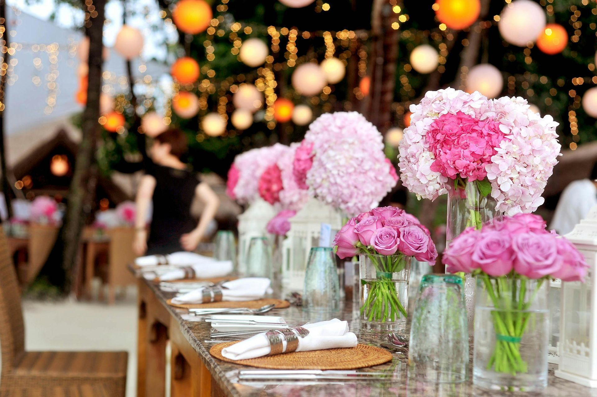 Una mesa larga preparada para una recepción de boda con flores rosas en jarrones.