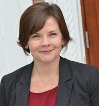 A woman in a black jacket and red shirt is smiling for the camera.
