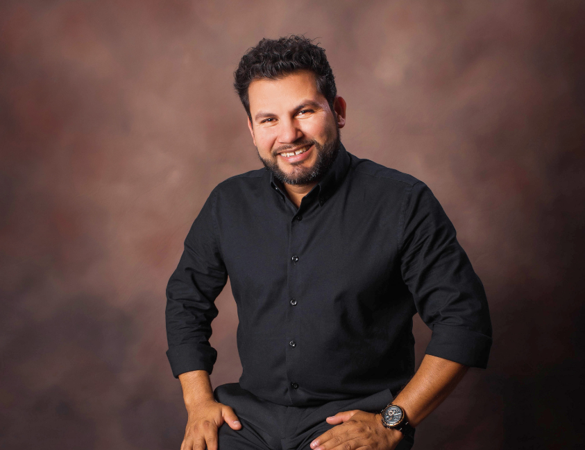 A man with a beard is wearing a black shirt and a watch.