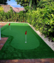 A small green putting green in a backyard with a red flag.