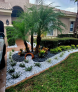 A car is parked in front of a house in a lush green yard.