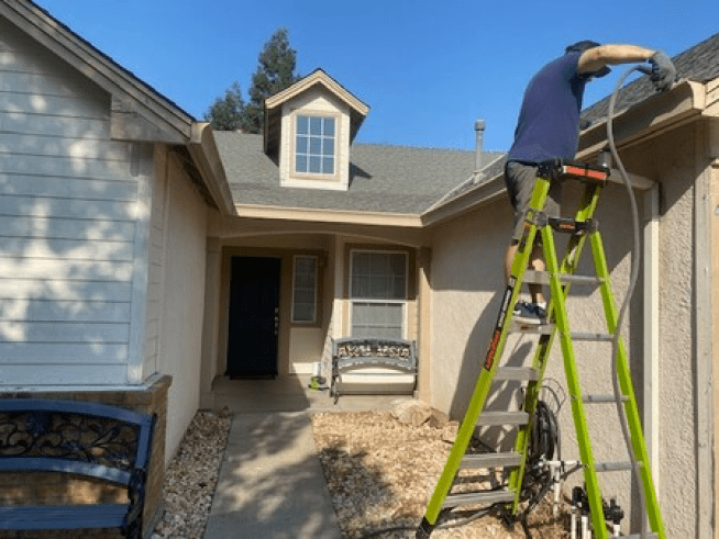 A man on a ladder working on the roof of a house