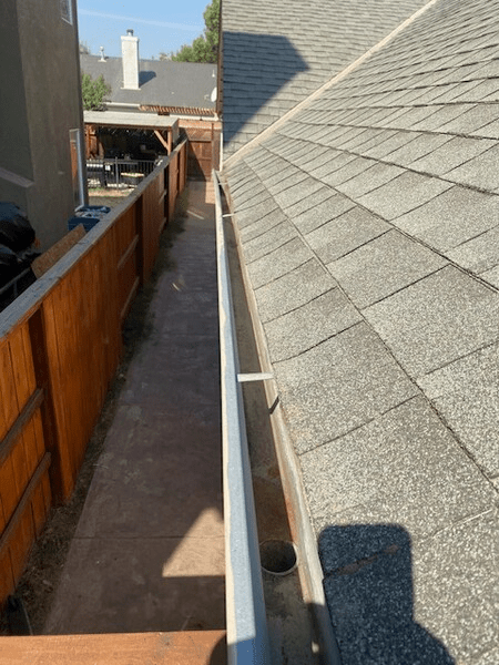 A gutter on the side of a house next to a wooden fence.