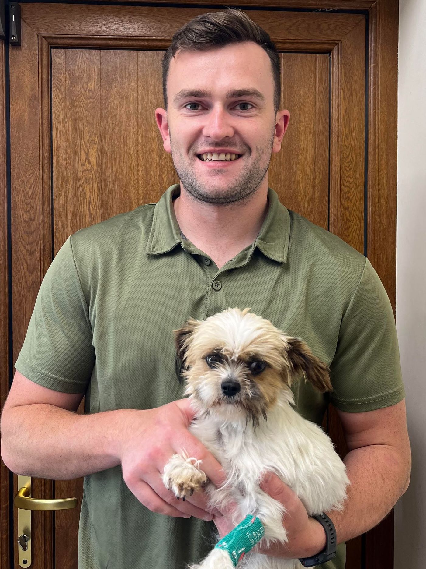 A man in a green shirt is holding a small white dog