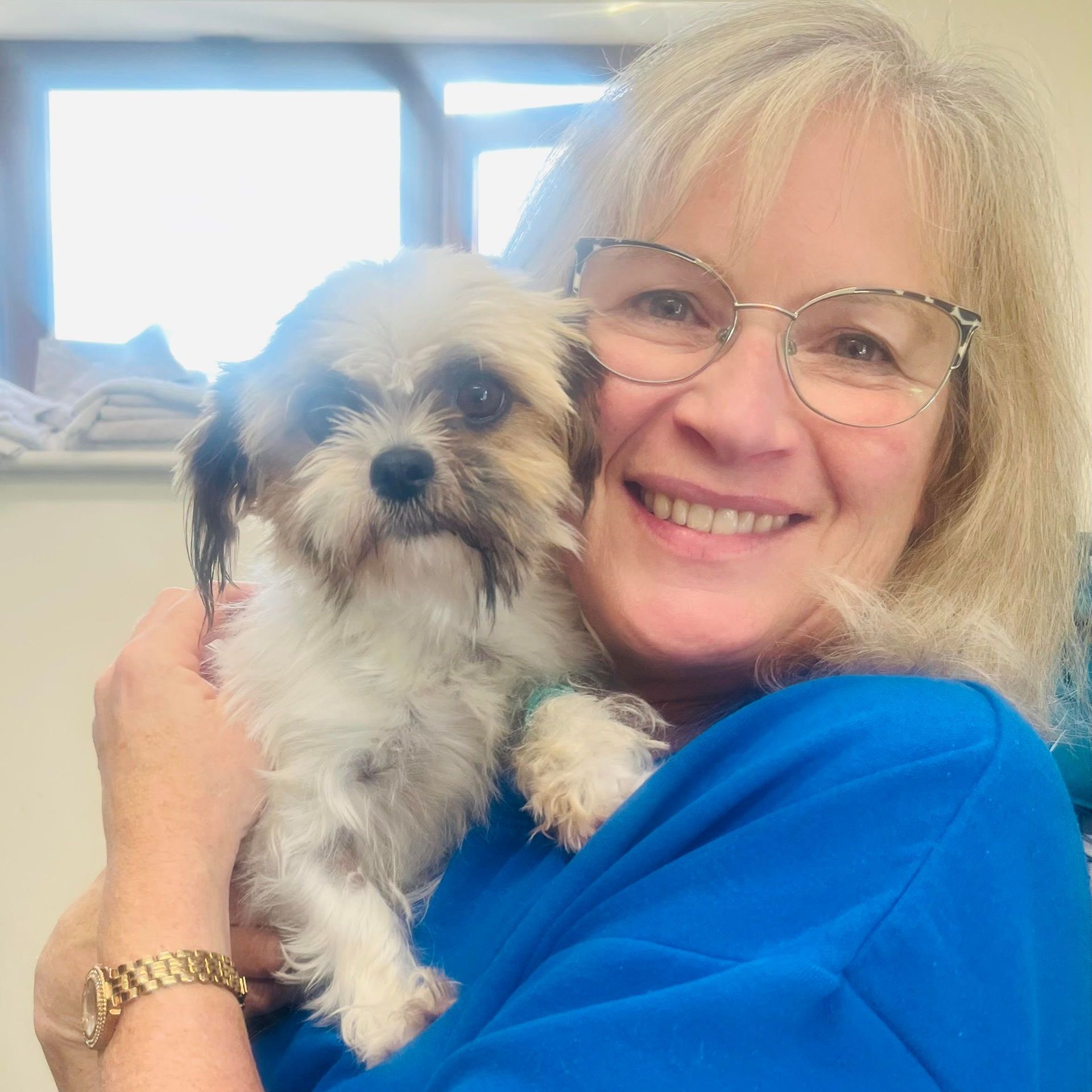 A woman wearing glasses is holding a small dog in her arms.