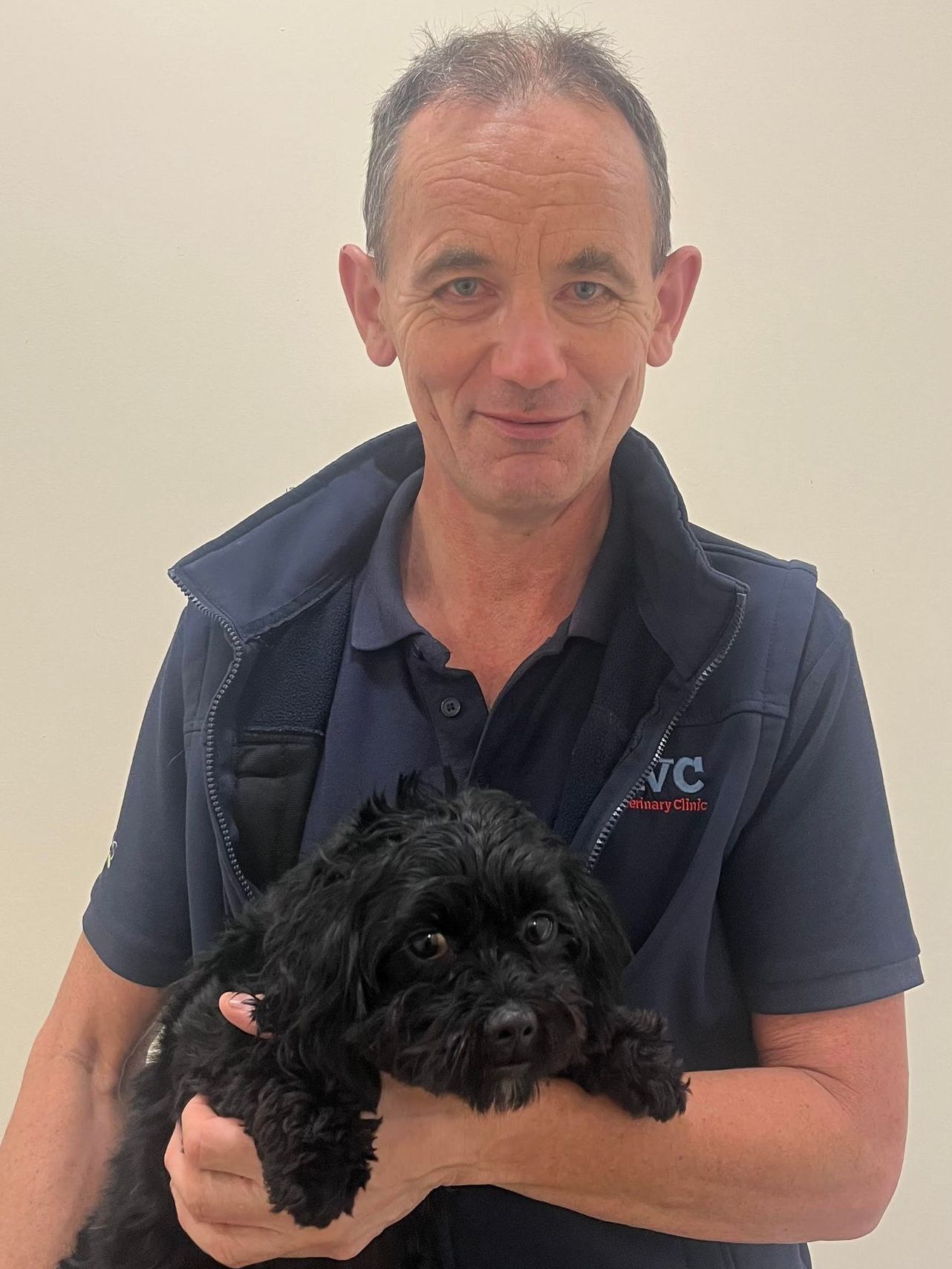 A man in a blue shirt is holding a small black dog.