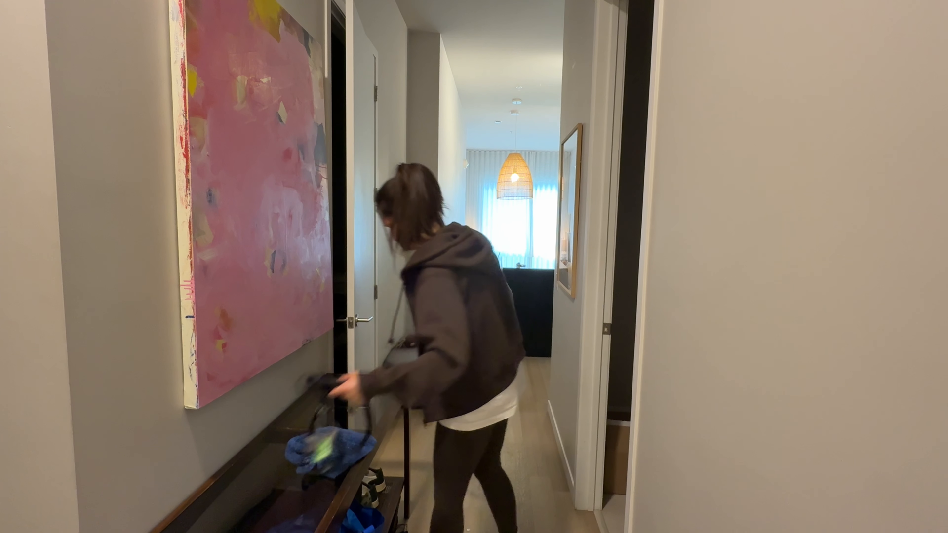 Man vacuums a rug in a modern living room with a large window and neutral decor.
