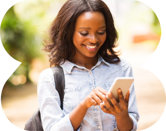 A woman is smiling while looking at her cell phone.