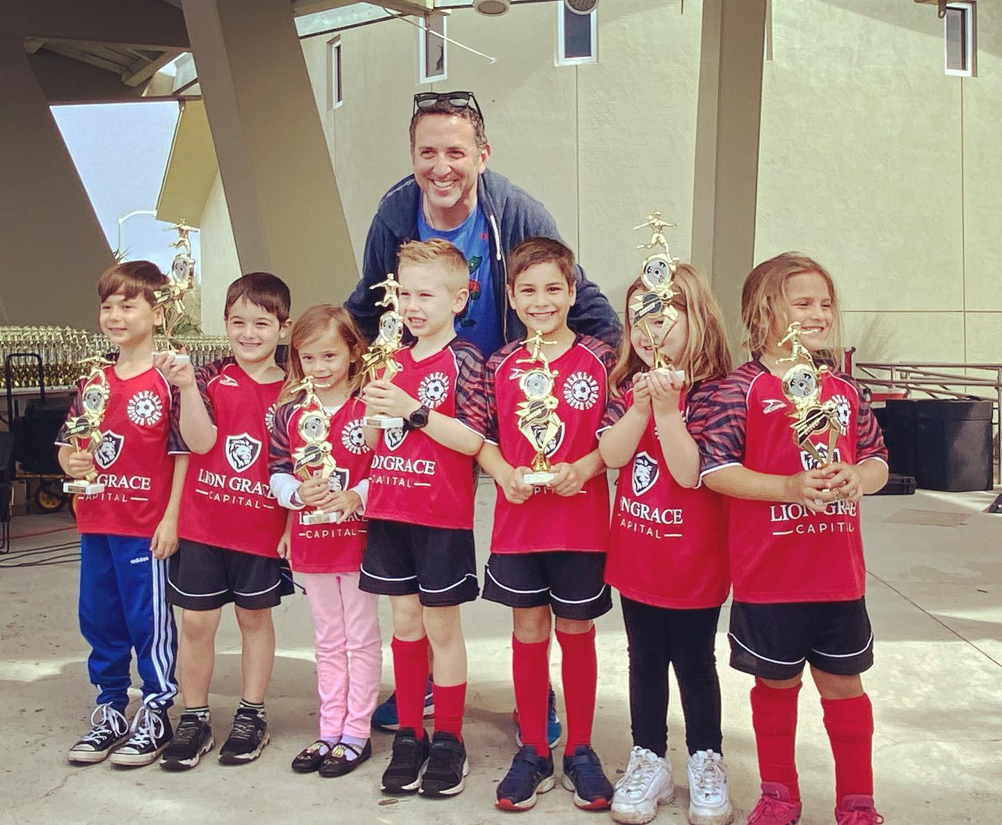 A group of young children holding trophies with a man standing behind them
