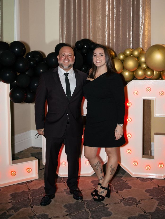 A man and a woman are posing for a picture in front of a large letter l.
