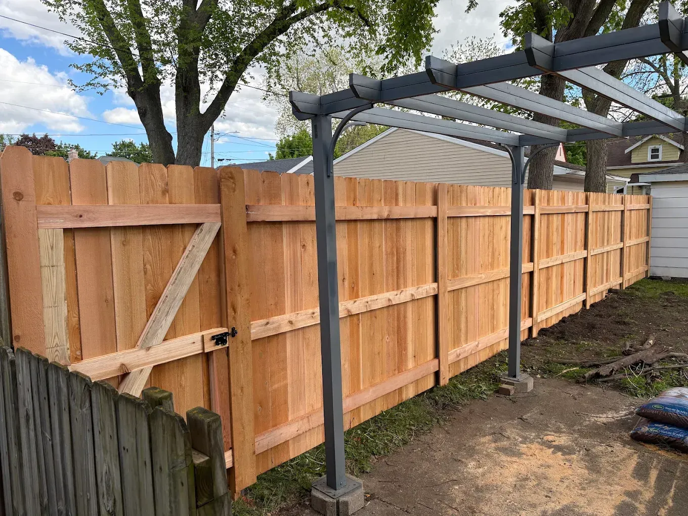 A new wooden fence with gate in a backyard, supported by grey posts and pergola.
