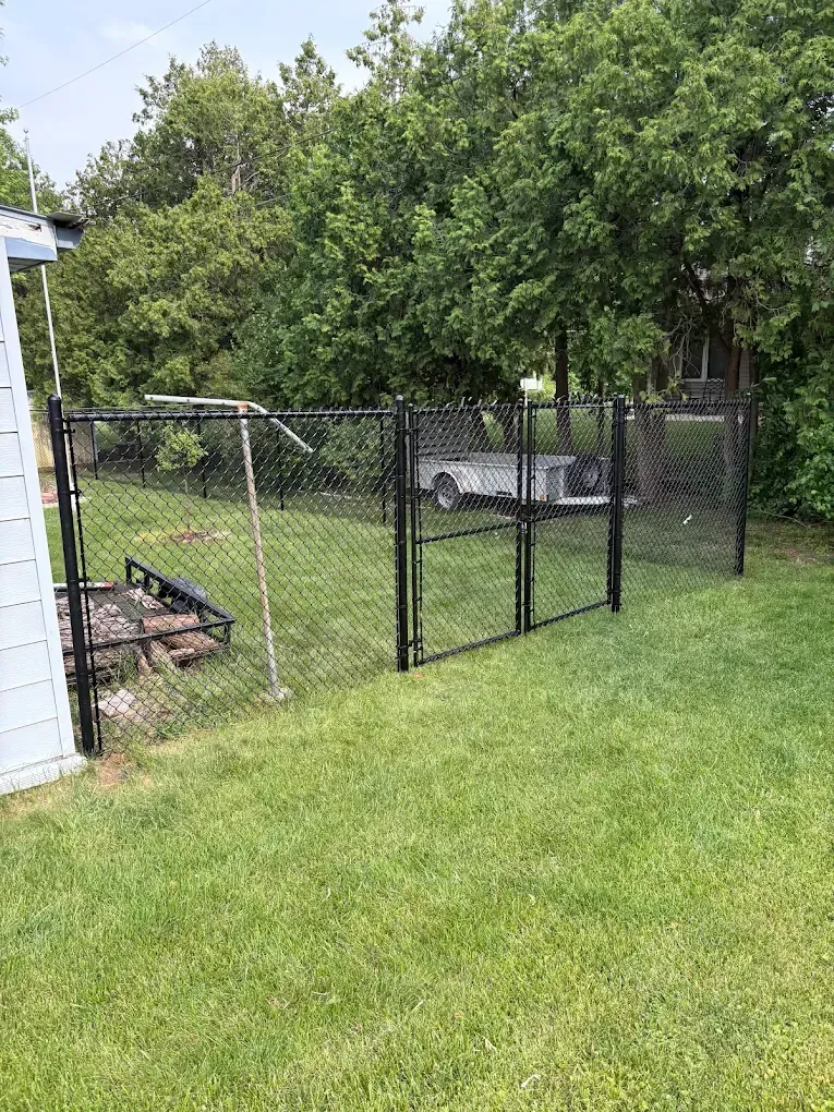 Black chain-link fence in backyard with two gates; trailer visible behind the fence.