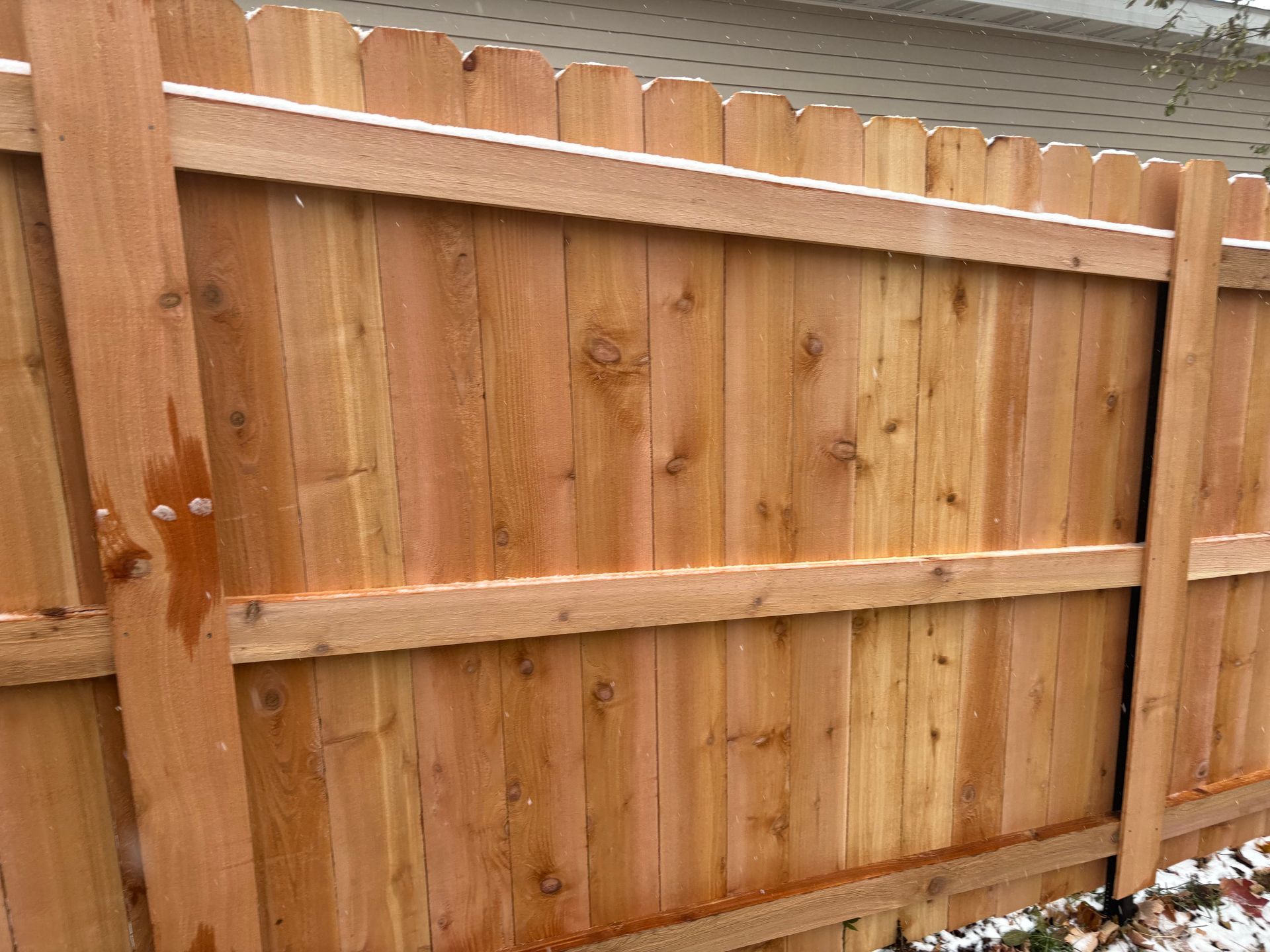 Wooden fence with vertical planks, horizontal rails, and a scalloped top, with snow.