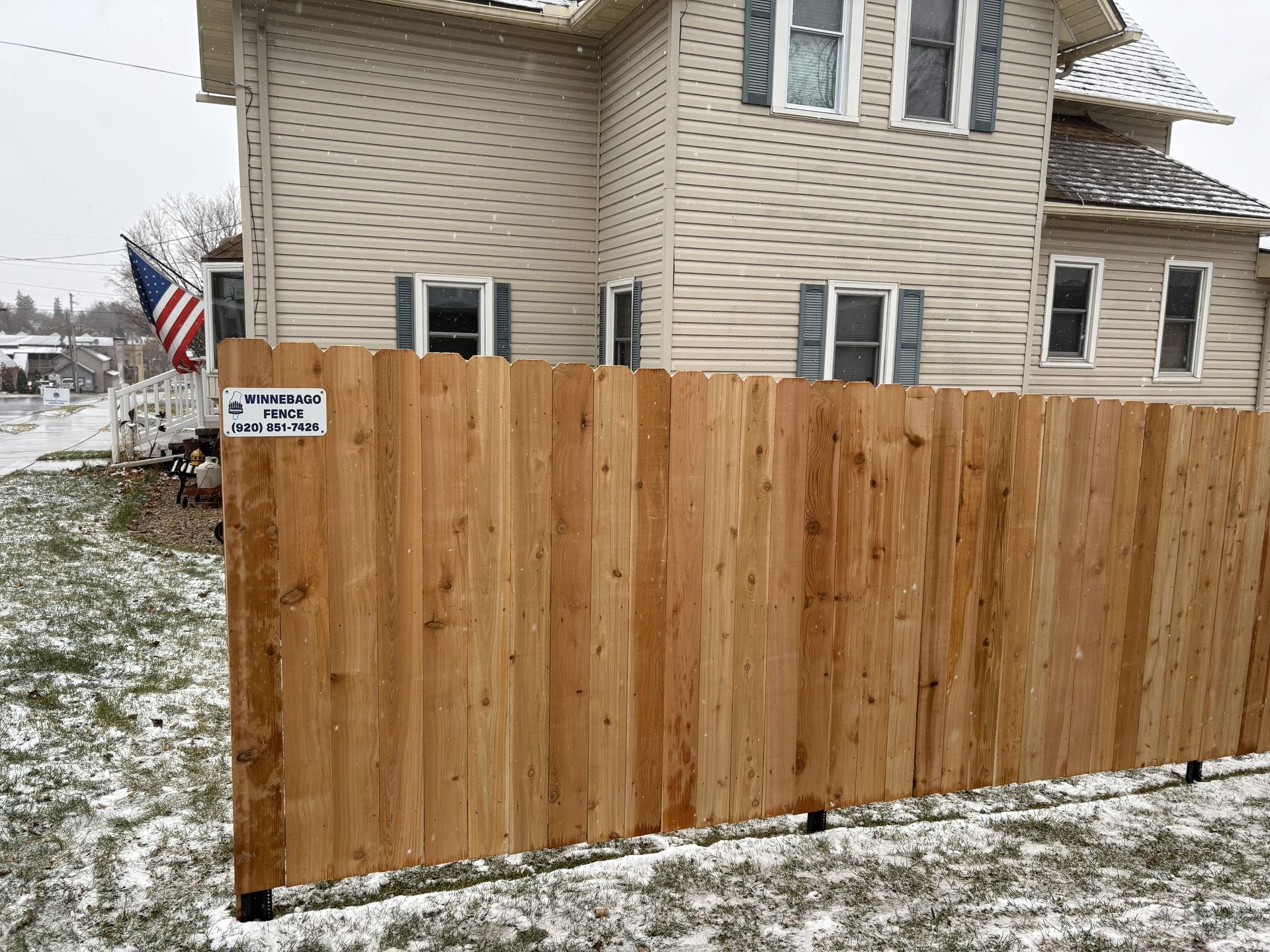 Wooden fence in front of a house, snow on the ground.