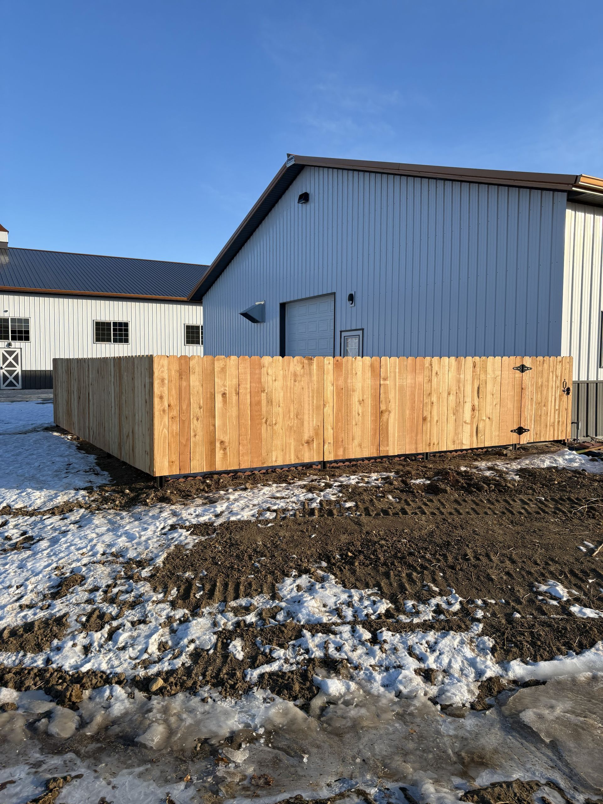Wooden fence in front of a white building with a black roof and snow-covered ground.