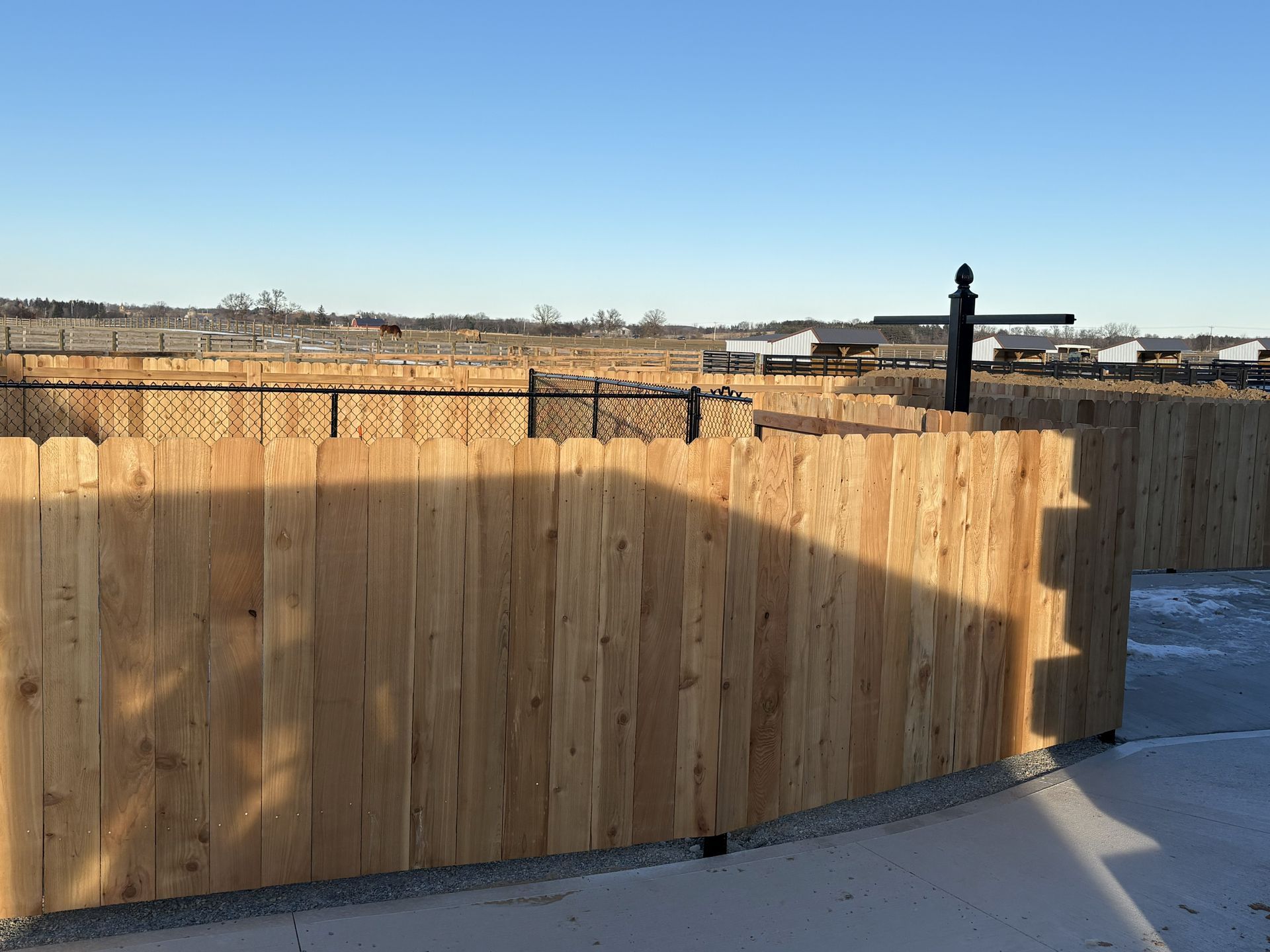 Wooden fence with a chain-link fence behind it, under a clear blue sky.