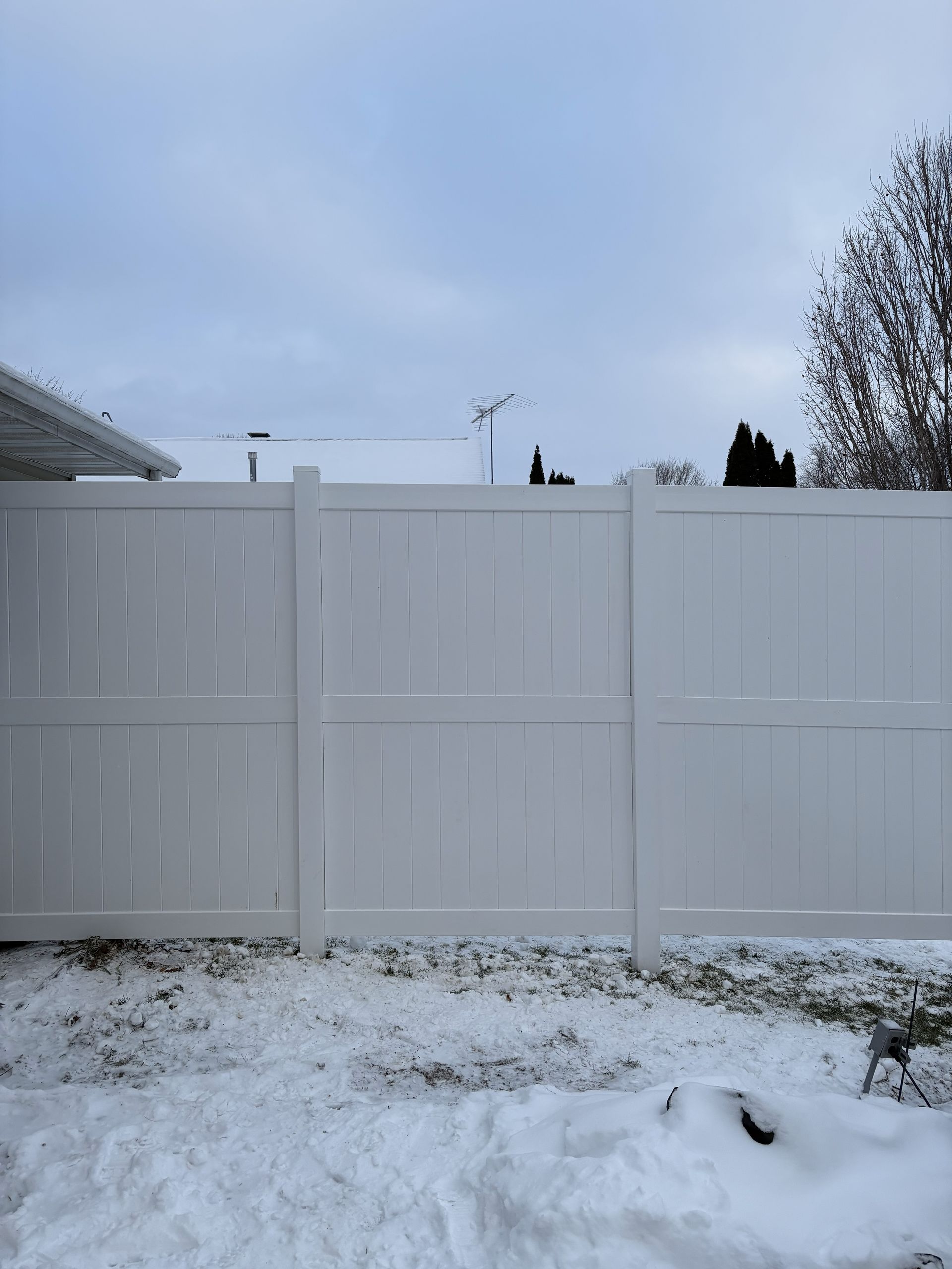 White vinyl fence in snowy yard under a cloudy sky.