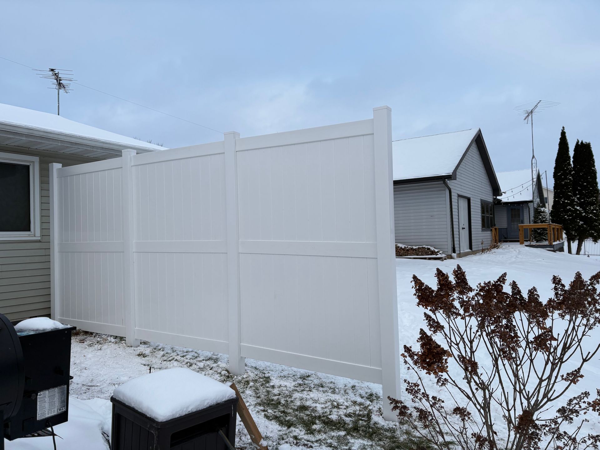 White vinyl fence in snowy backyard with a house in the background.