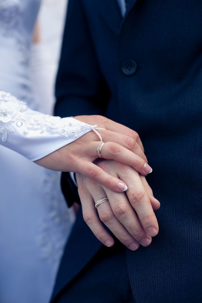 A Bride and Groom Are Holding Hands With Their Wedding Rings on — K. Smith & Son Jewellers In Caloundra, QLD