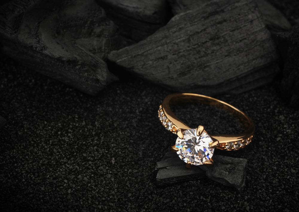 A Gold Ring With a Diamond in the Center is Sitting on a Piece of Coal — K. Smith & Son Jewellers In Caloundra, QLD