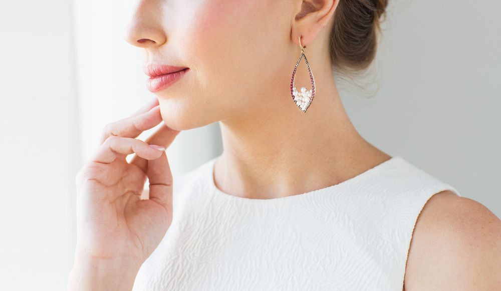 A Woman Wearing a White Dress and Earrings is Touching Her Face — K. Smith & Son Jewellers In Caloundra, QLD