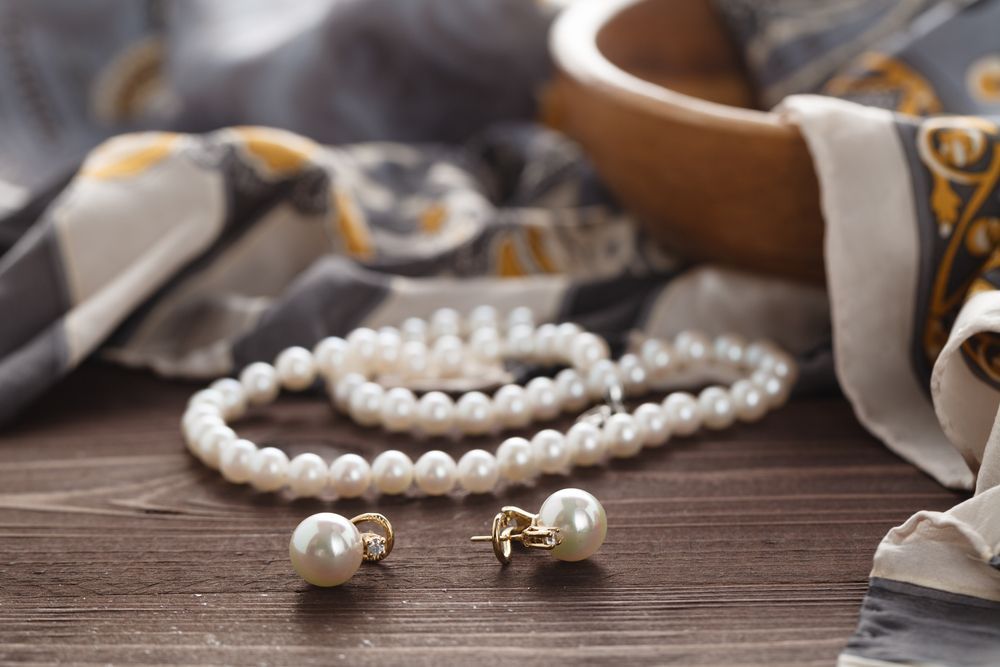 A Pearl Necklace, Earrings, and Scarf Are on a Wooden Table — K. Smith & Son Jewellers In Caloundra, QLD
