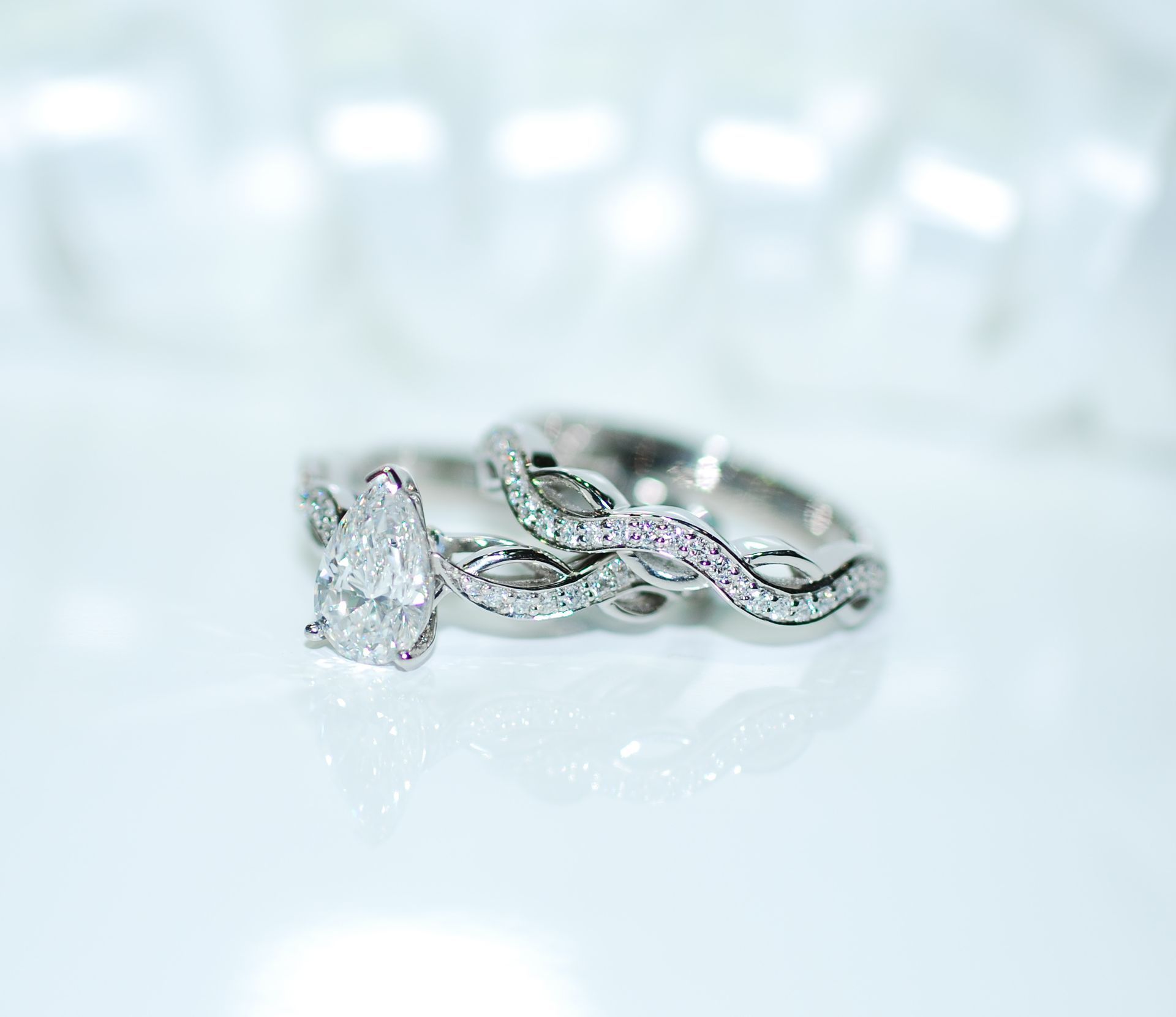 Pear-shaped diamond engagement ring and matching diamond band on a white surface, intertwined design — K. Smith & Son Jewellers In Caloundra, QLD