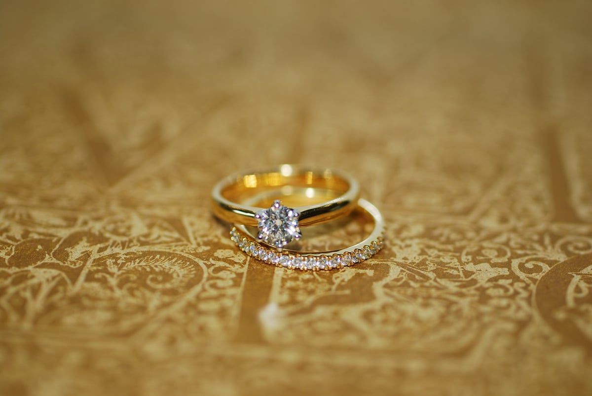 Two Gold Wedding Rings, One with A Large Central Diamond, on A Patterned Brown Surface  — K. Smith & Son Jewellers In Caloundra, QLD