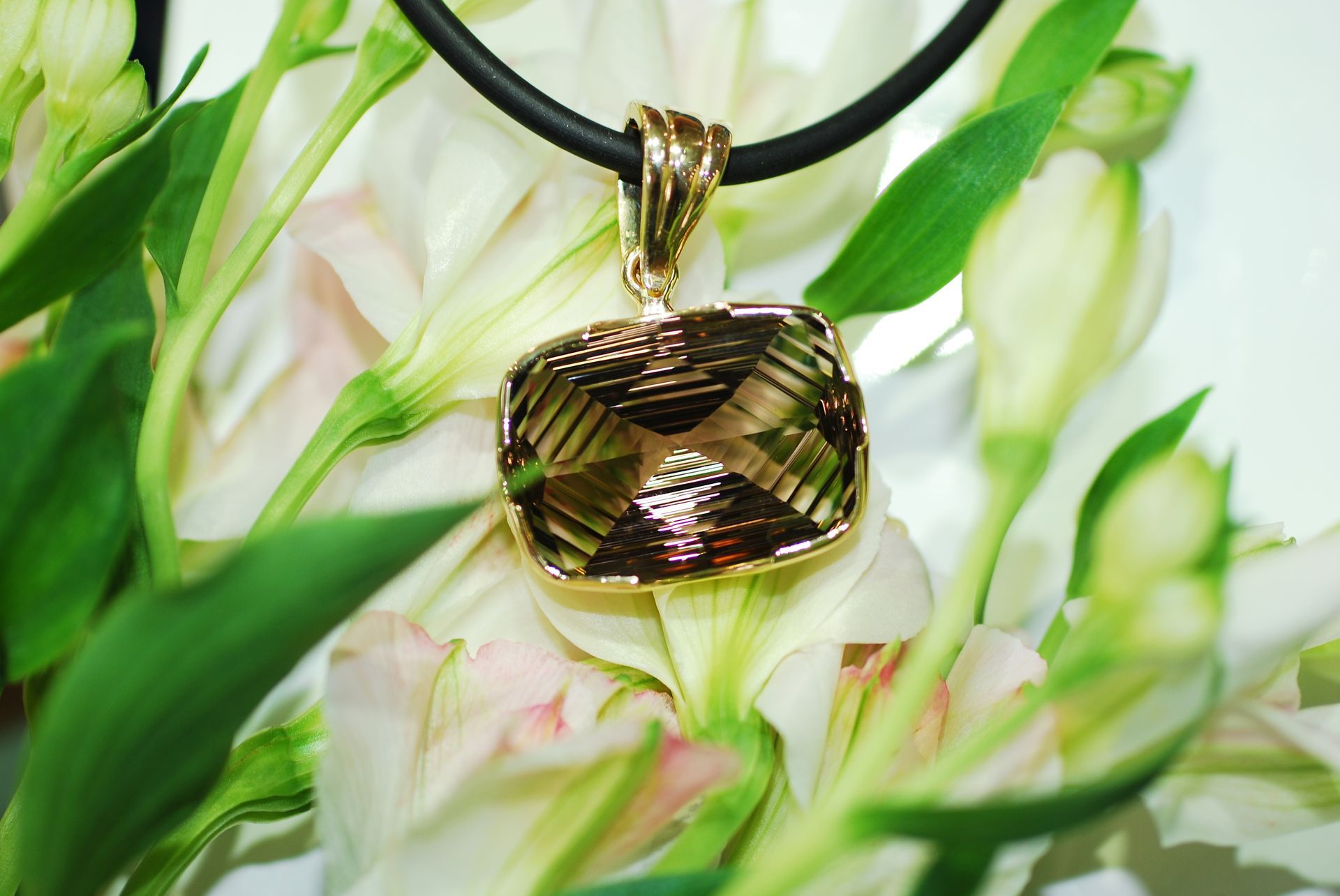 Gold pendant with a large brown gemstone on a black cord, set against white and green flowers — K. Smith & Son Jewellers In Caloundra, QLD