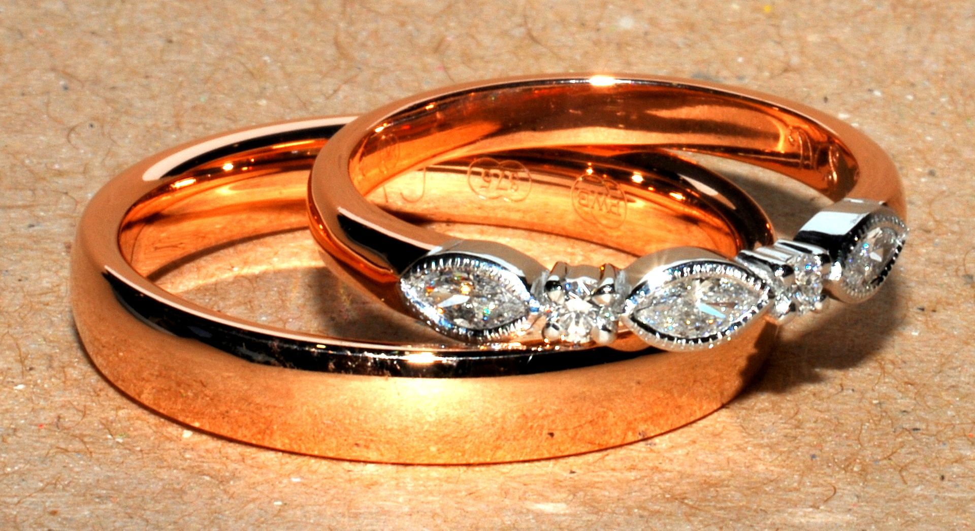 Two rose gold wedding rings, one with diamonds, on a textured surface — K. Smith & Son Jewellers In Caloundra, QLD