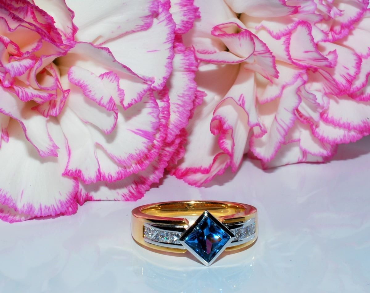 A Gold Ring With a Blue Stone is Sitting Next to a Pink Flower — K. Smith & Son Jewellers In Caloundra, QLD
