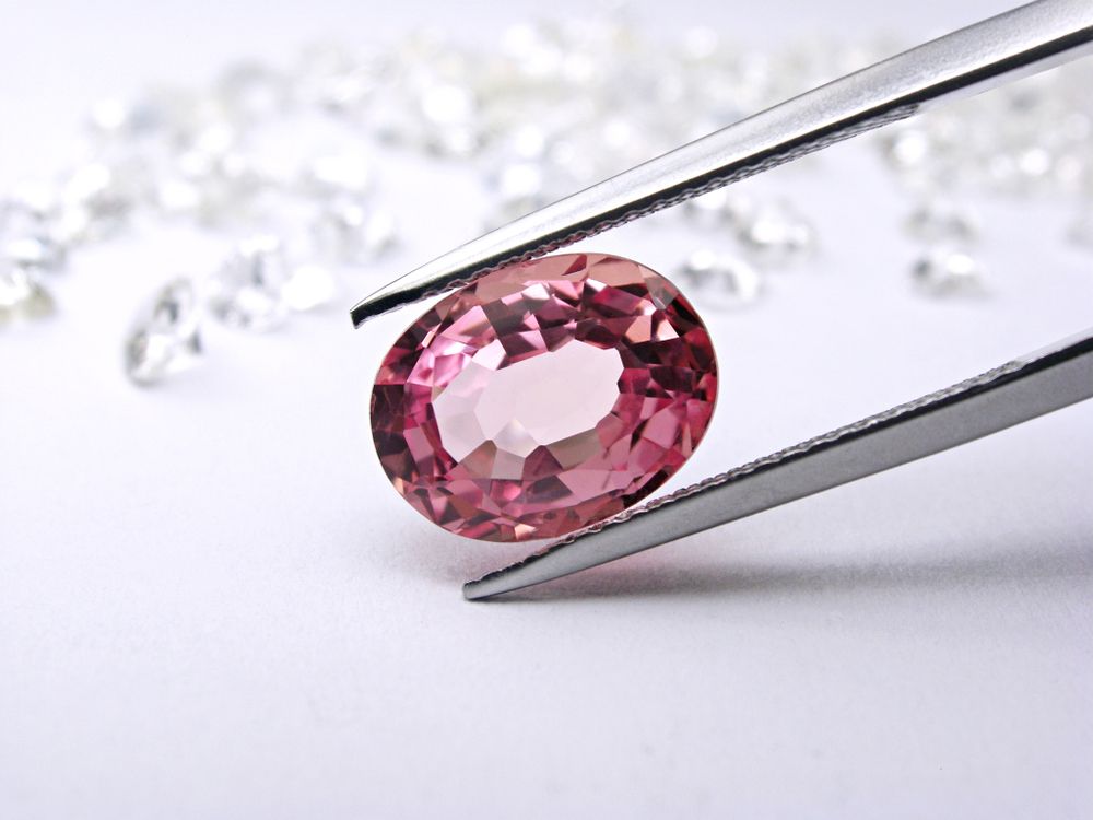 A Pink Stone is Being Held by Tweezers on a White Surface — K. Smith & Son Jewellers In Caloundra, QLD