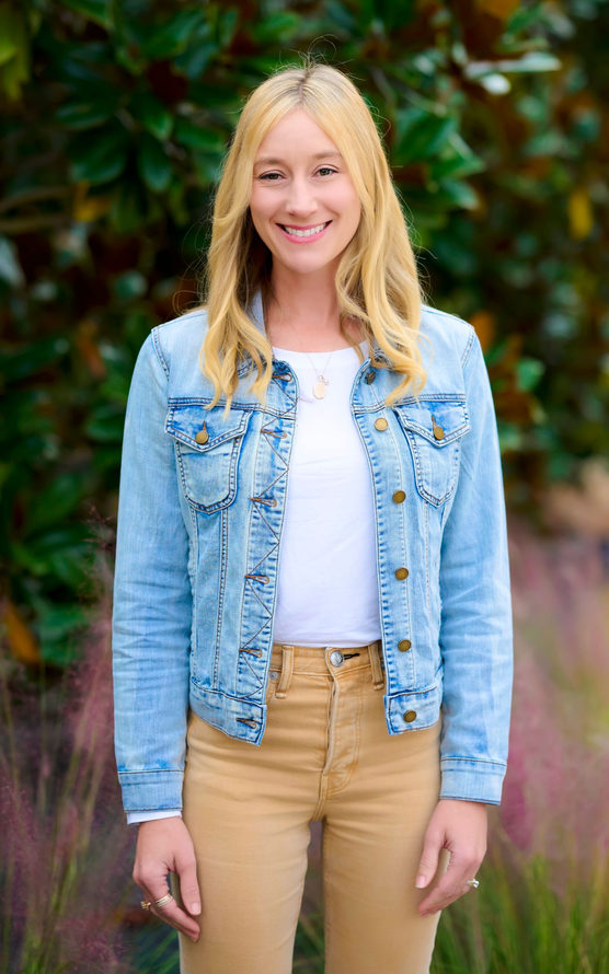 Morgan Larkin smiles, wearing a light denim jacket, white shirt, tan pants, outside.