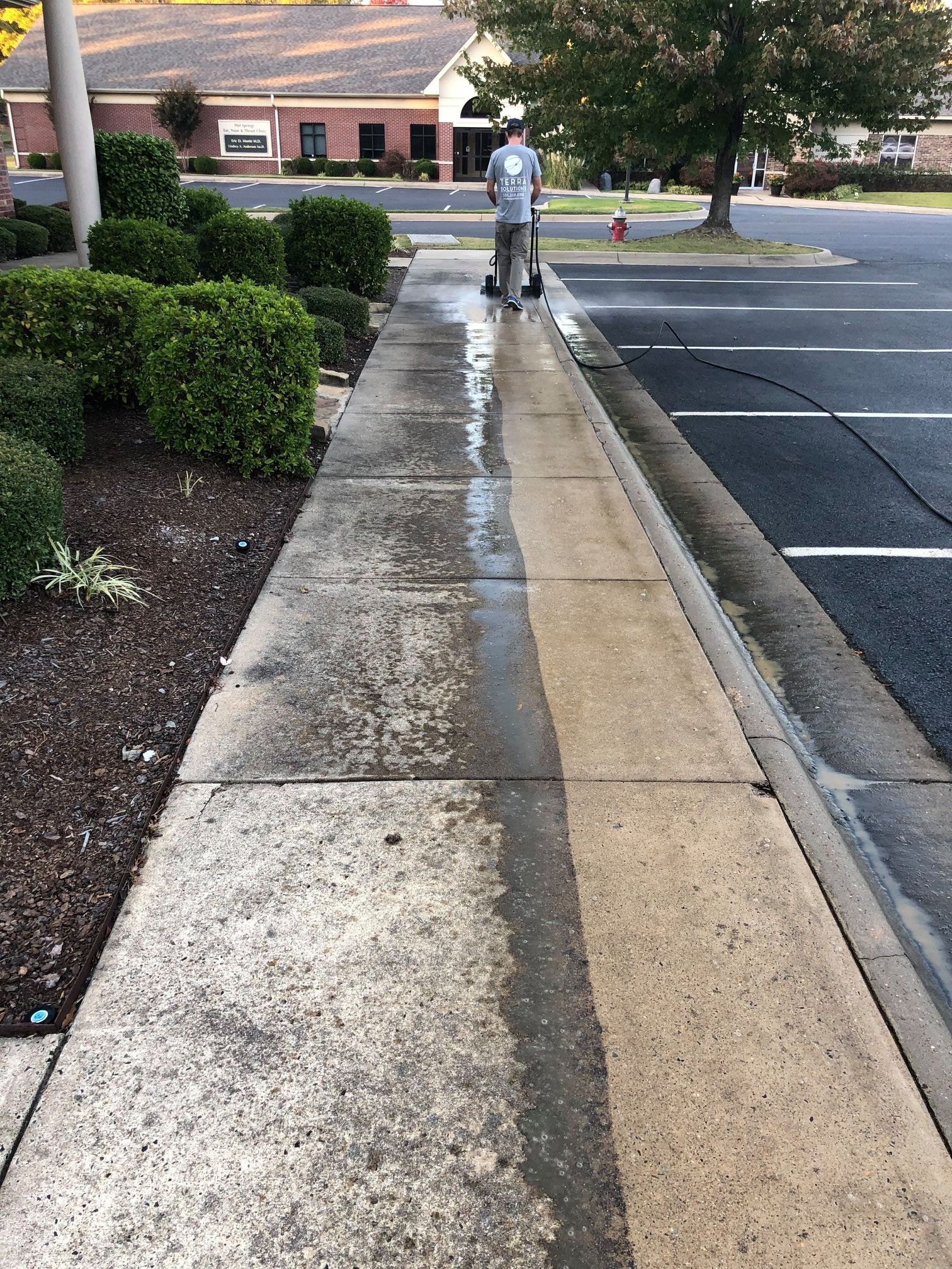A man is cleaning a sidewalk next to a parking lot.