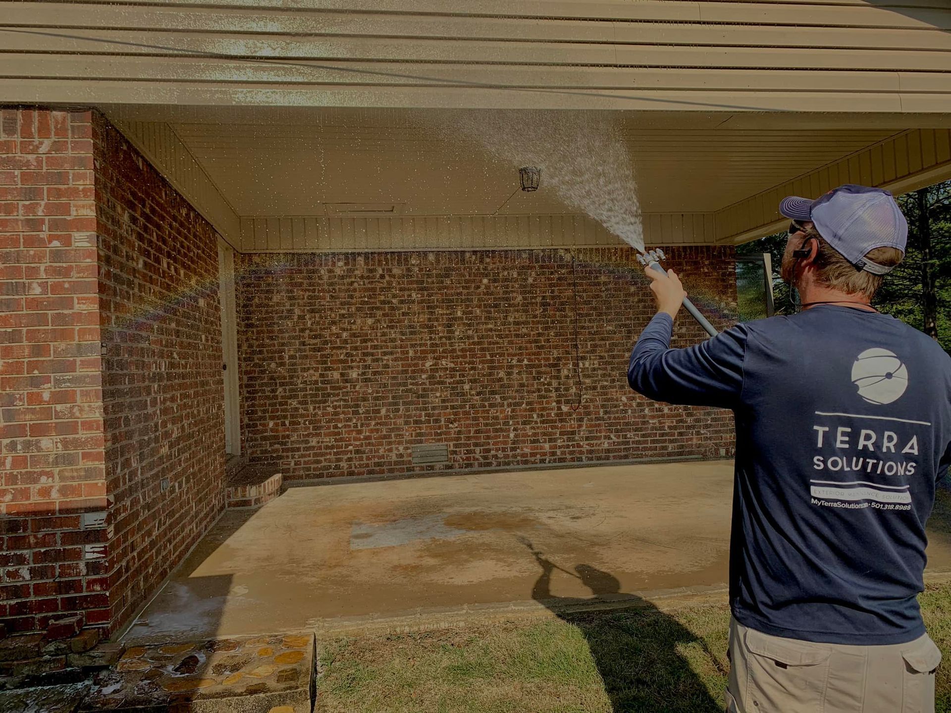 A man is spraying water on a brick wall with a hose.