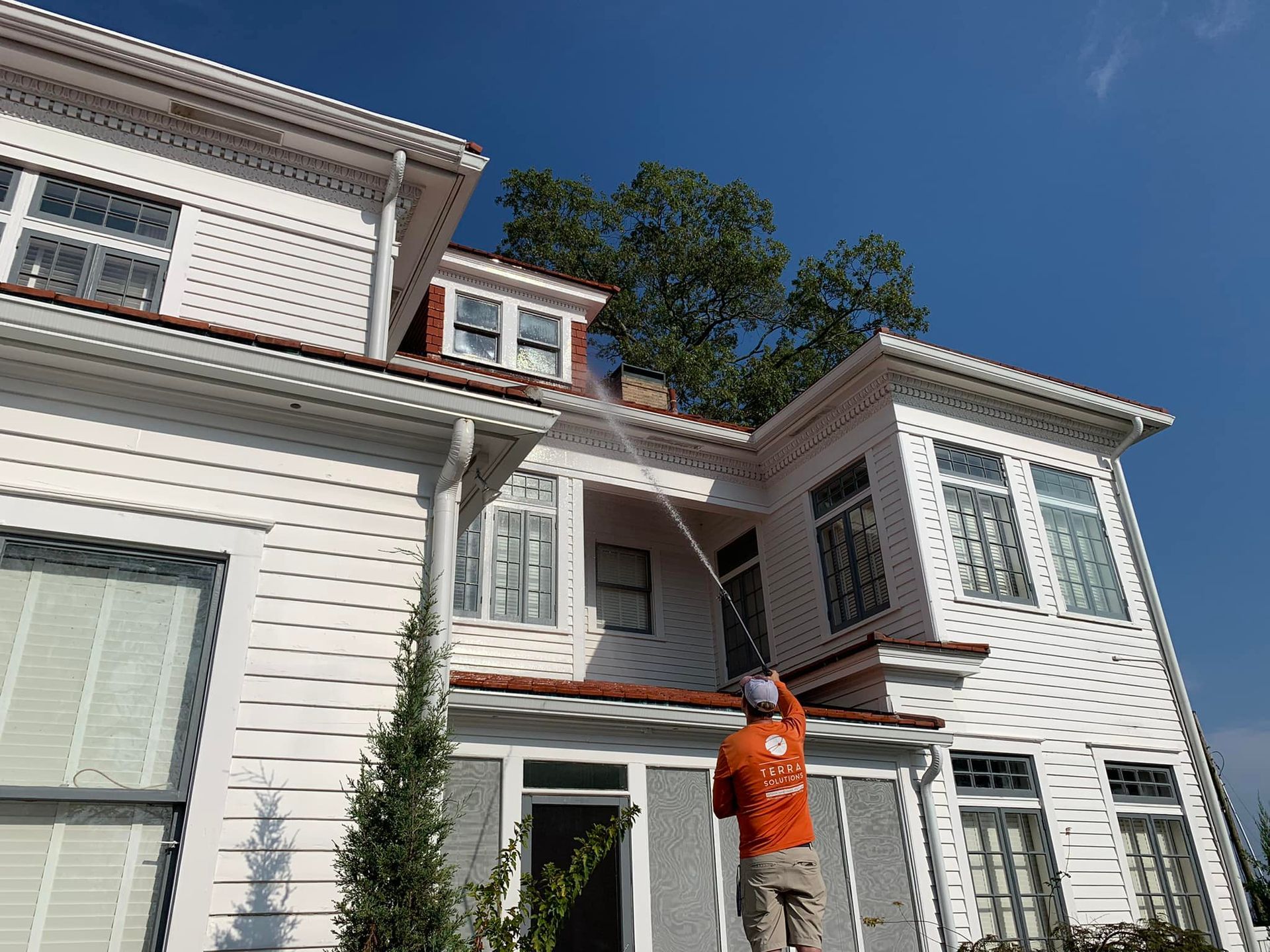 A man is cleaning the roof of a white house.