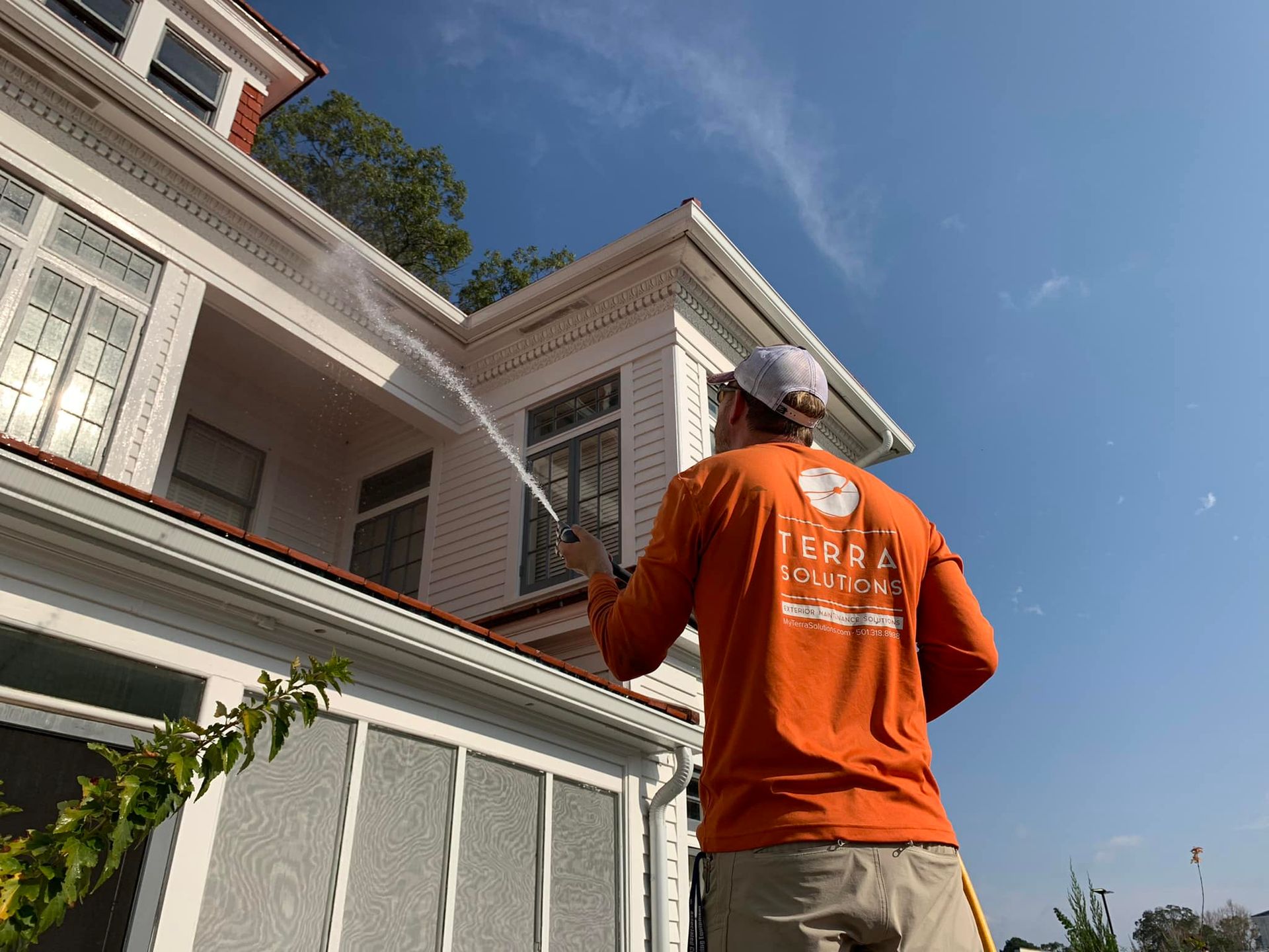 A man is cleaning the side of a house with a pressure washer.