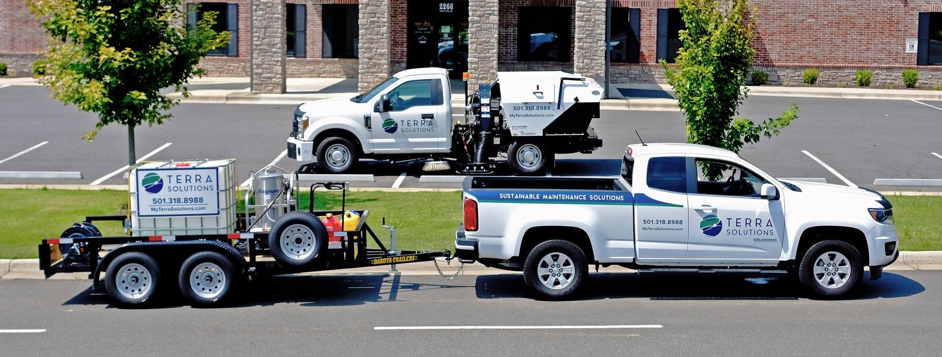 Two trucks are parked in a parking lot and one has a trailer attached to it