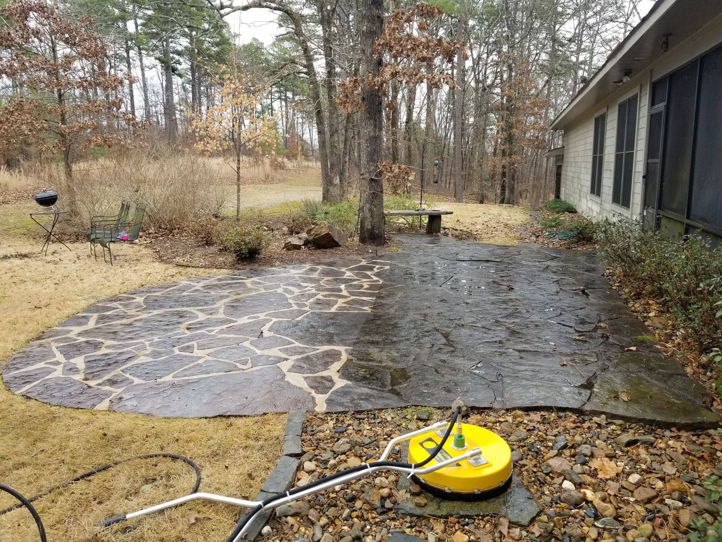 A patio is being cleaned with a pressure washer in front of a house.
