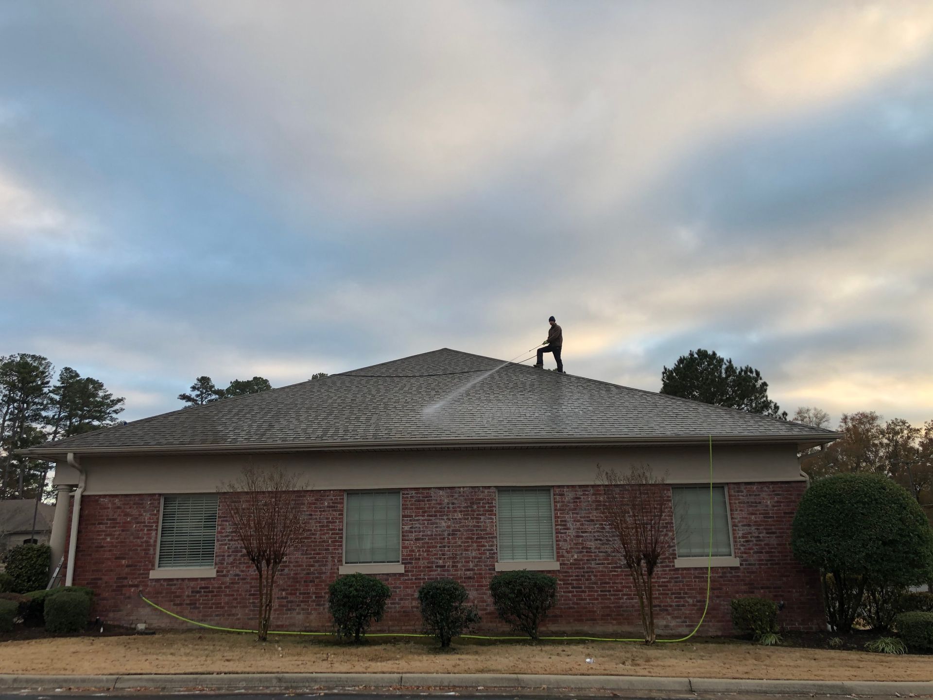 A man is standing on the roof of a brick house.