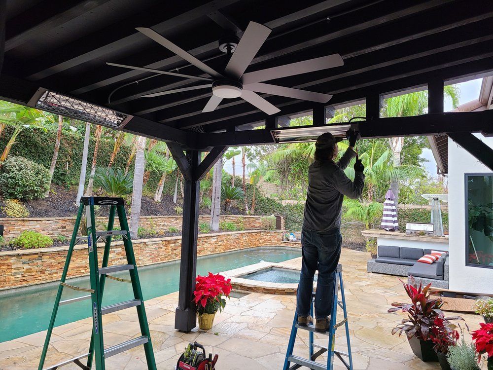 A man is standing on a ladder fixing a ceiling fan.