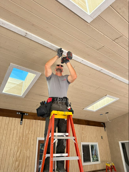 A man is standing on a ladder working on a ceiling
