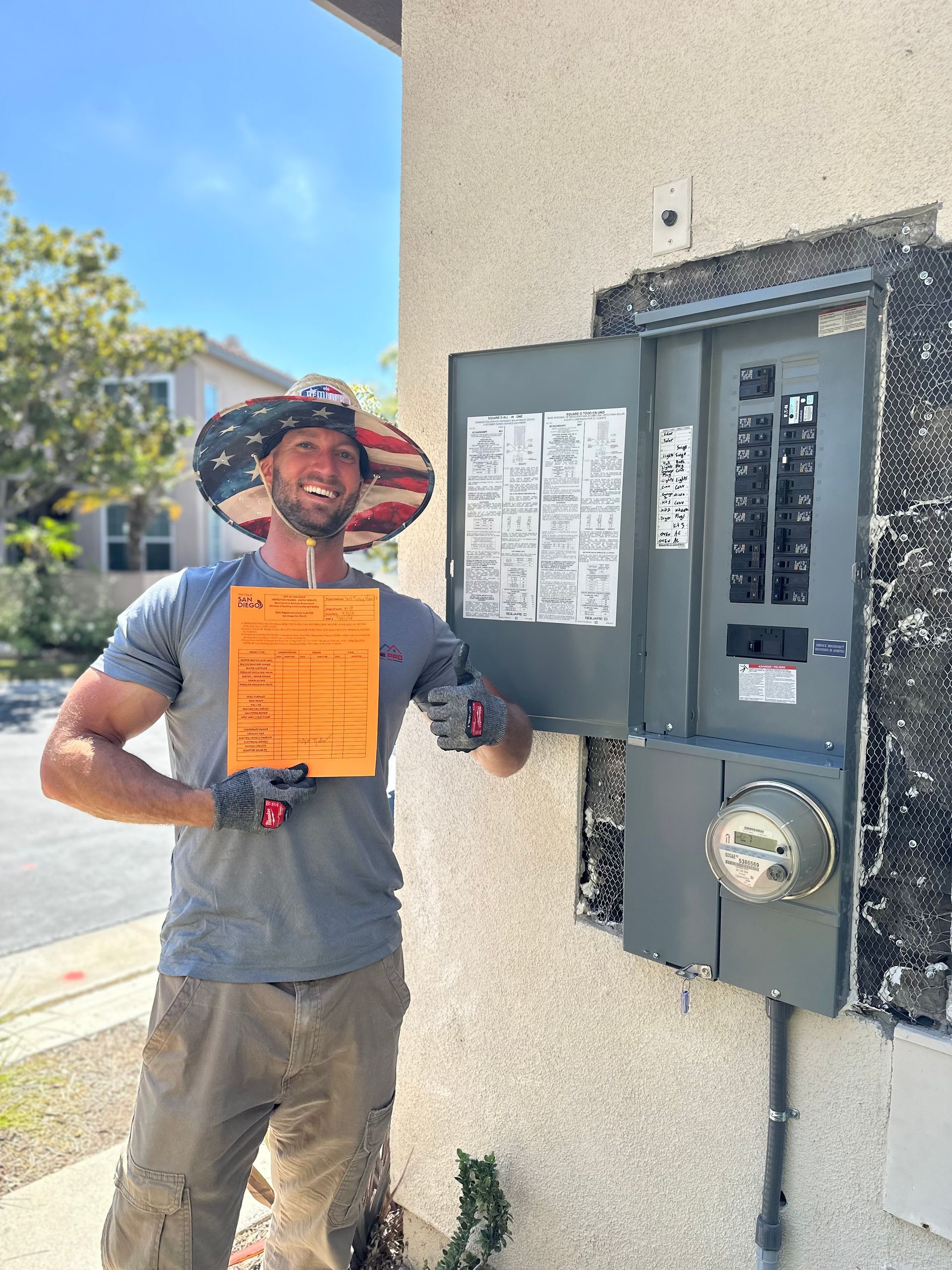 A man wearing an american flag hat is standing in front of an electrical box holding a certificate.