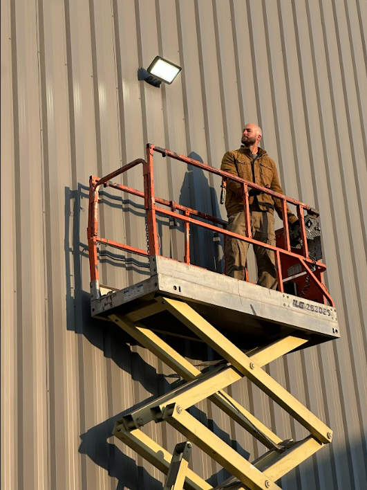 A man is standing on a scissor lift in front of a building.