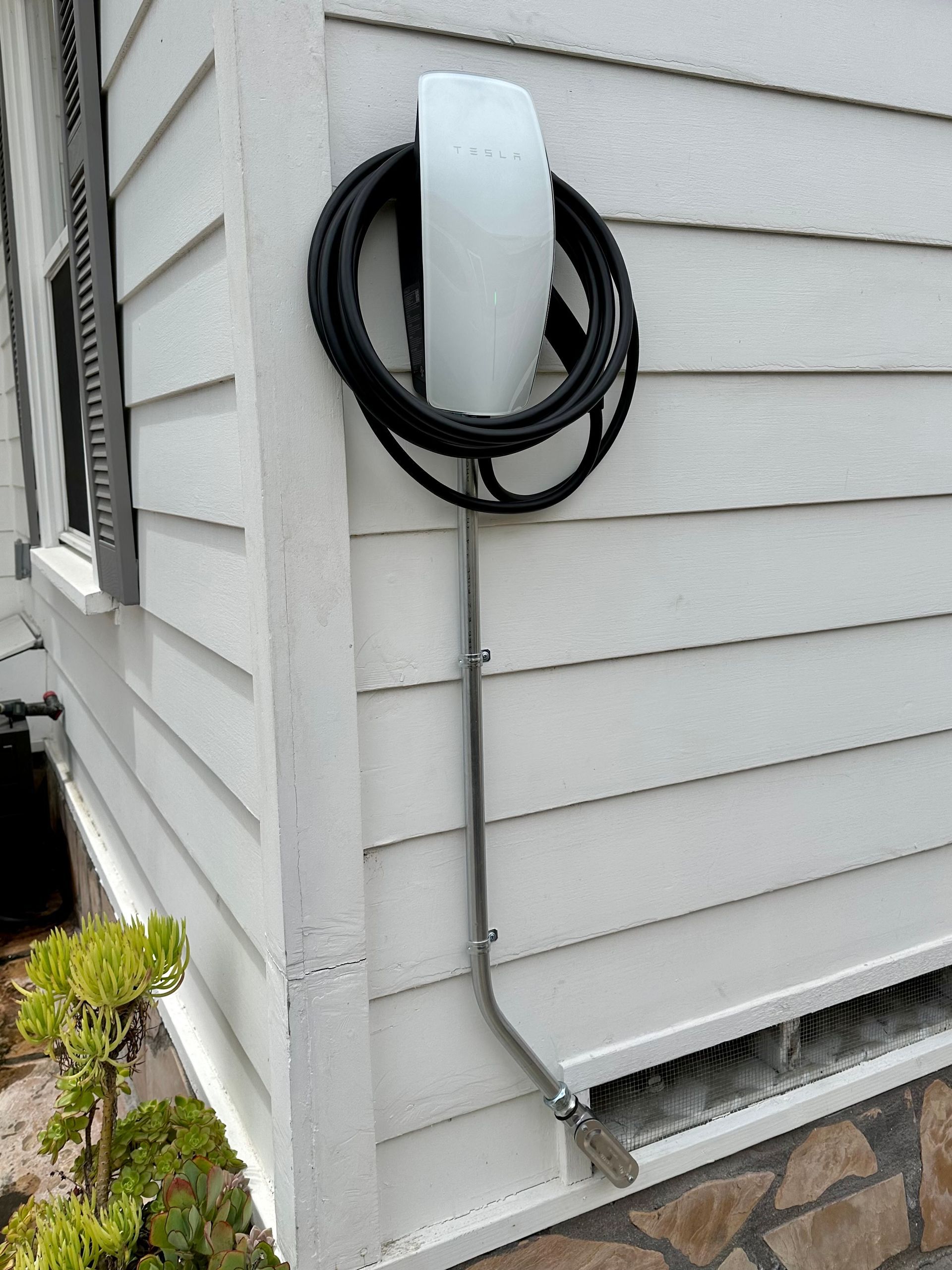 A tesla charging station is attached to the side of a house.