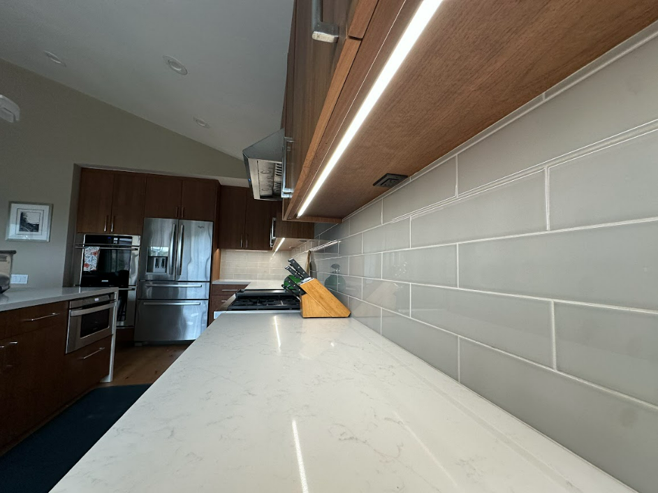 A kitchen with white counter tops , stainless steel appliances , and a refrigerator.