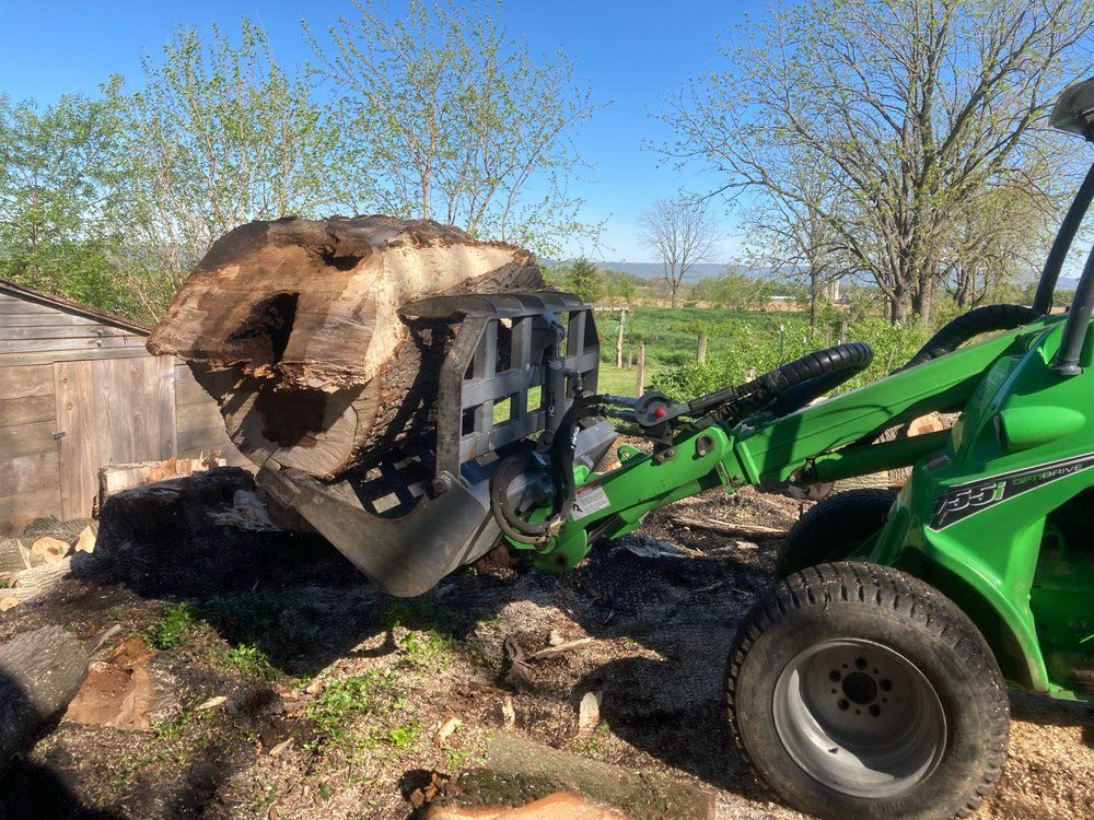 Green tractor with a log grapple holding a large piece of wood outdoors.